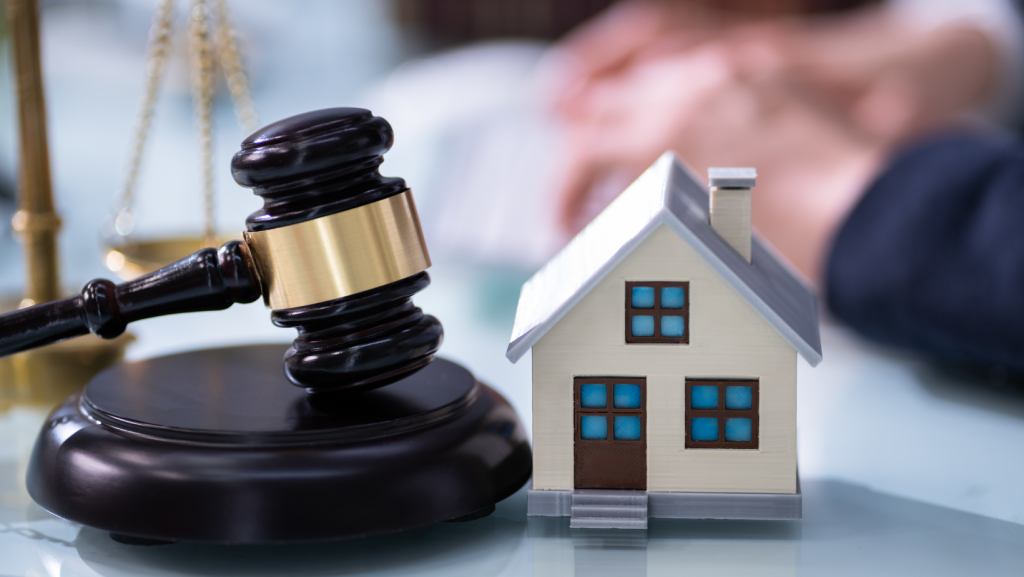 A wooden judge's gavel resting next to a model house and legal books, symbolizing real estate law and litigation.