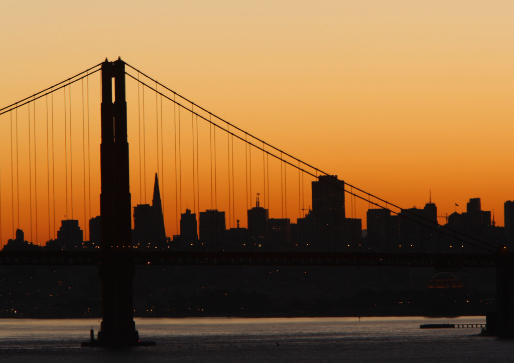 Silhouette of the Golden Gate Bridge and San Francisco skyline during a vibrant orange sunset.